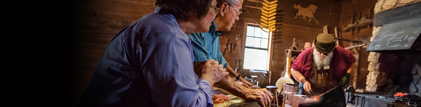 Coppia di anziani che osserva il fabbro mentre batte un pezzo di metallo presso il John Deere Historic Site a Grand Detour, Illinois, Stati Uniti