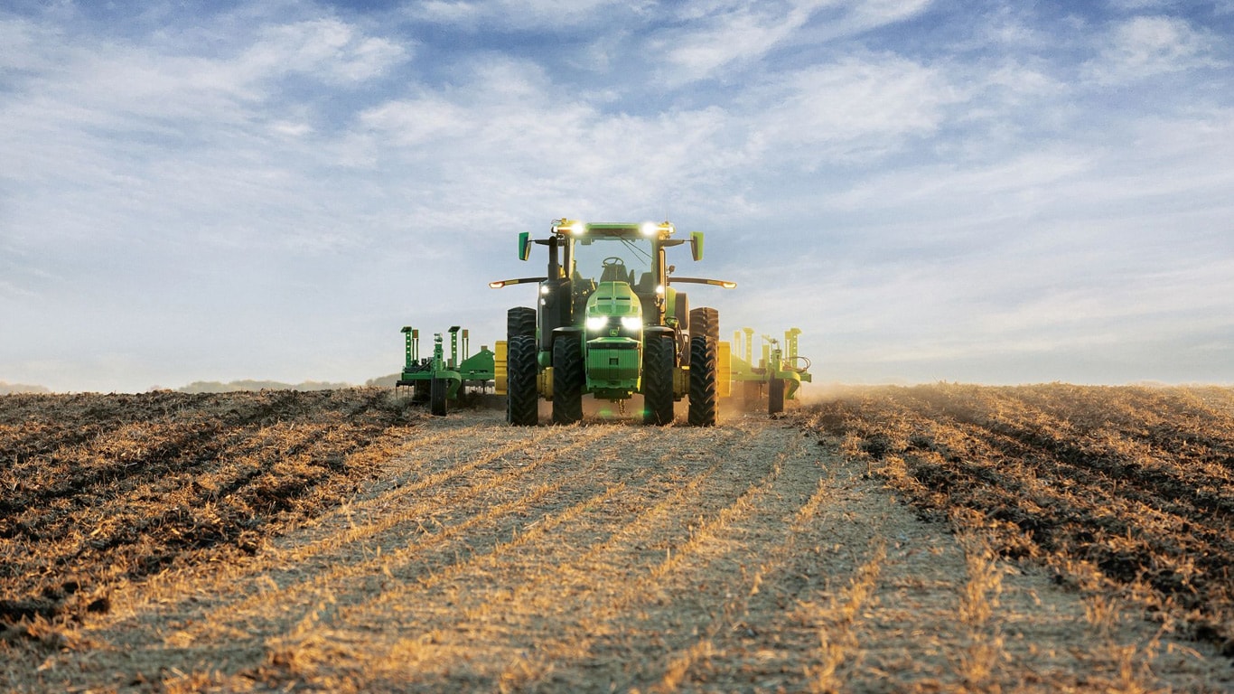 Trattore John Deere a guida autonoma che traina un macchinario per il dissodamento in un campo aperto.