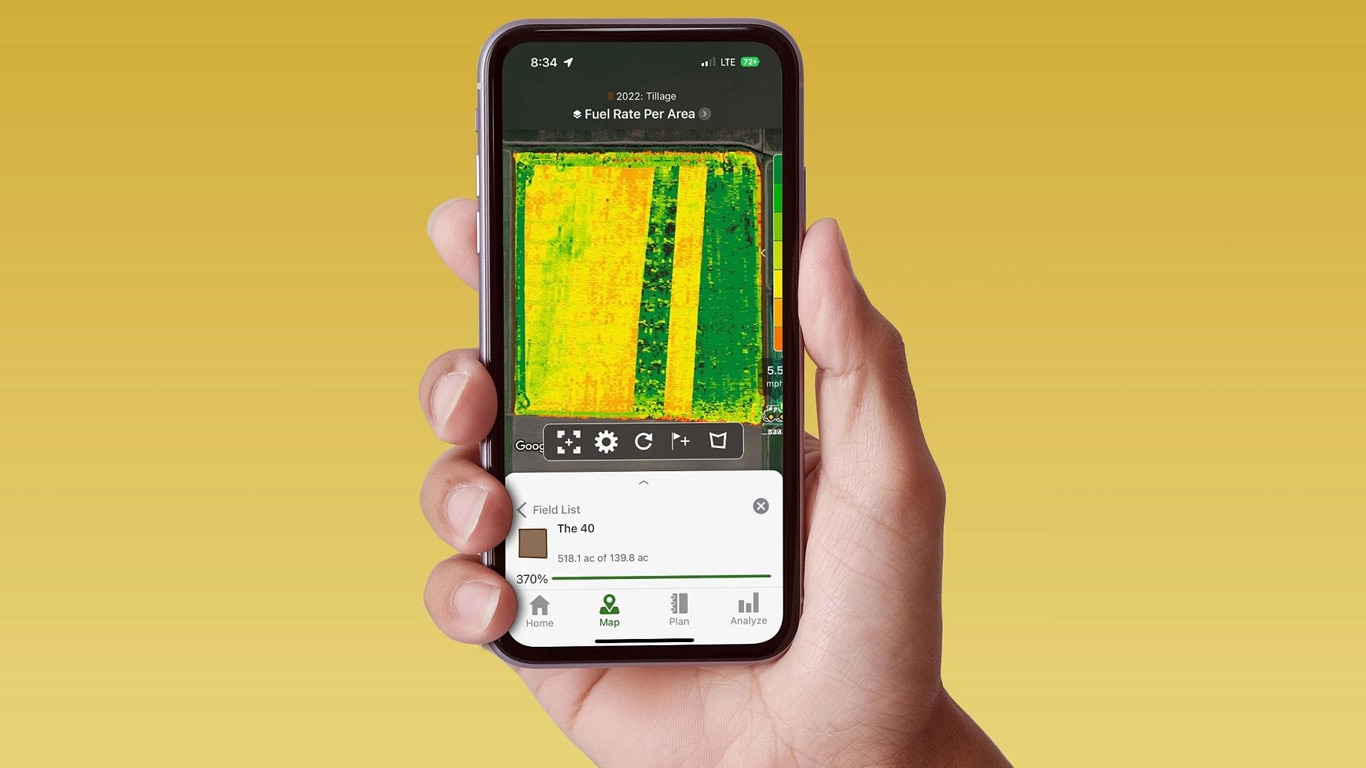 Mano che tiene uno smartphone su cui è visualizzato John Deere Operations Center con dati sul consumo di carburante.