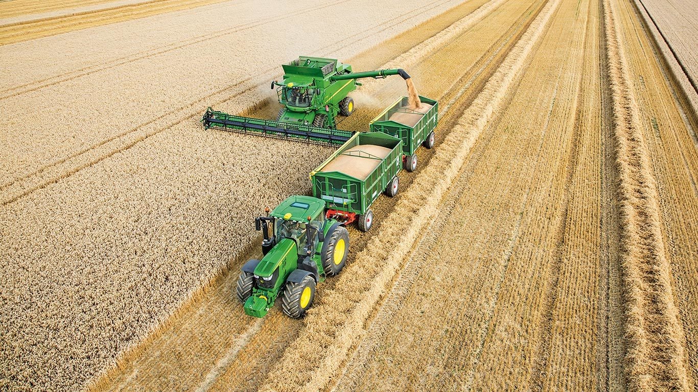 Mietitrebbia John Deere Serie S che scarica il grano su due rimorchi trainati da trattore