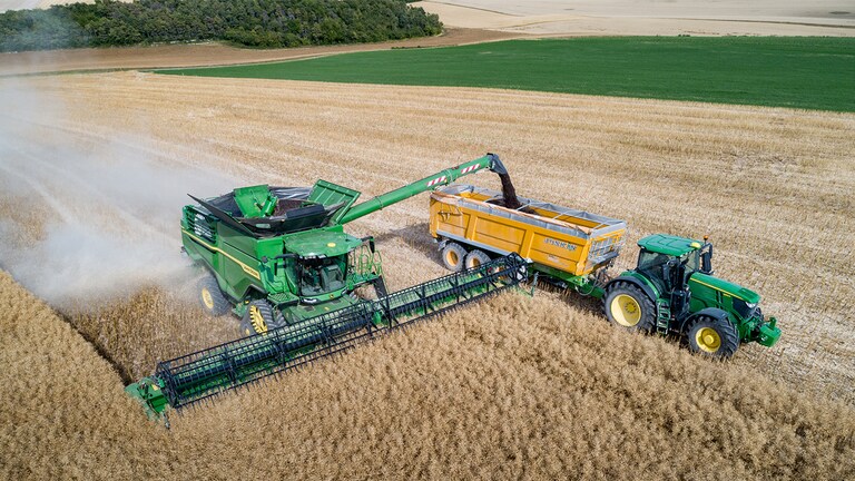 Mietitrebbia John Deere Serie X che scarica il semi di colza su un carro per la granella trainato da un trattore John Deere